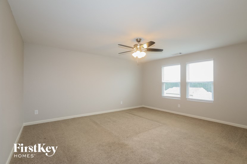 A room with a carpet floor, a ceiling fan, and two windows.