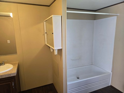 A white shower stall is in a bathroom with a sink and mirror.