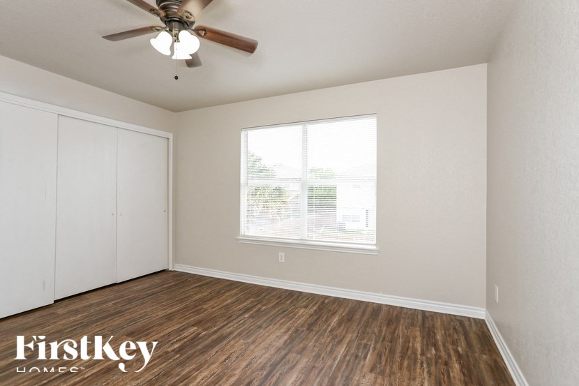 A room with a ceiling fan and a window with a view of a building outside.