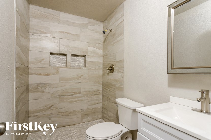 A bathroom with a marble tile shower and a white toilet.