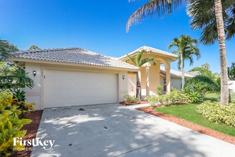 A house with a driveway and palm trees in front.