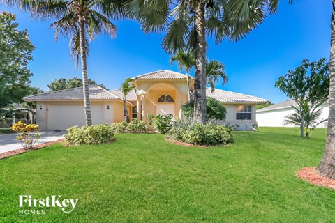 A house with a white exterior and a yellow roof is surrounded by greenery and palm trees.