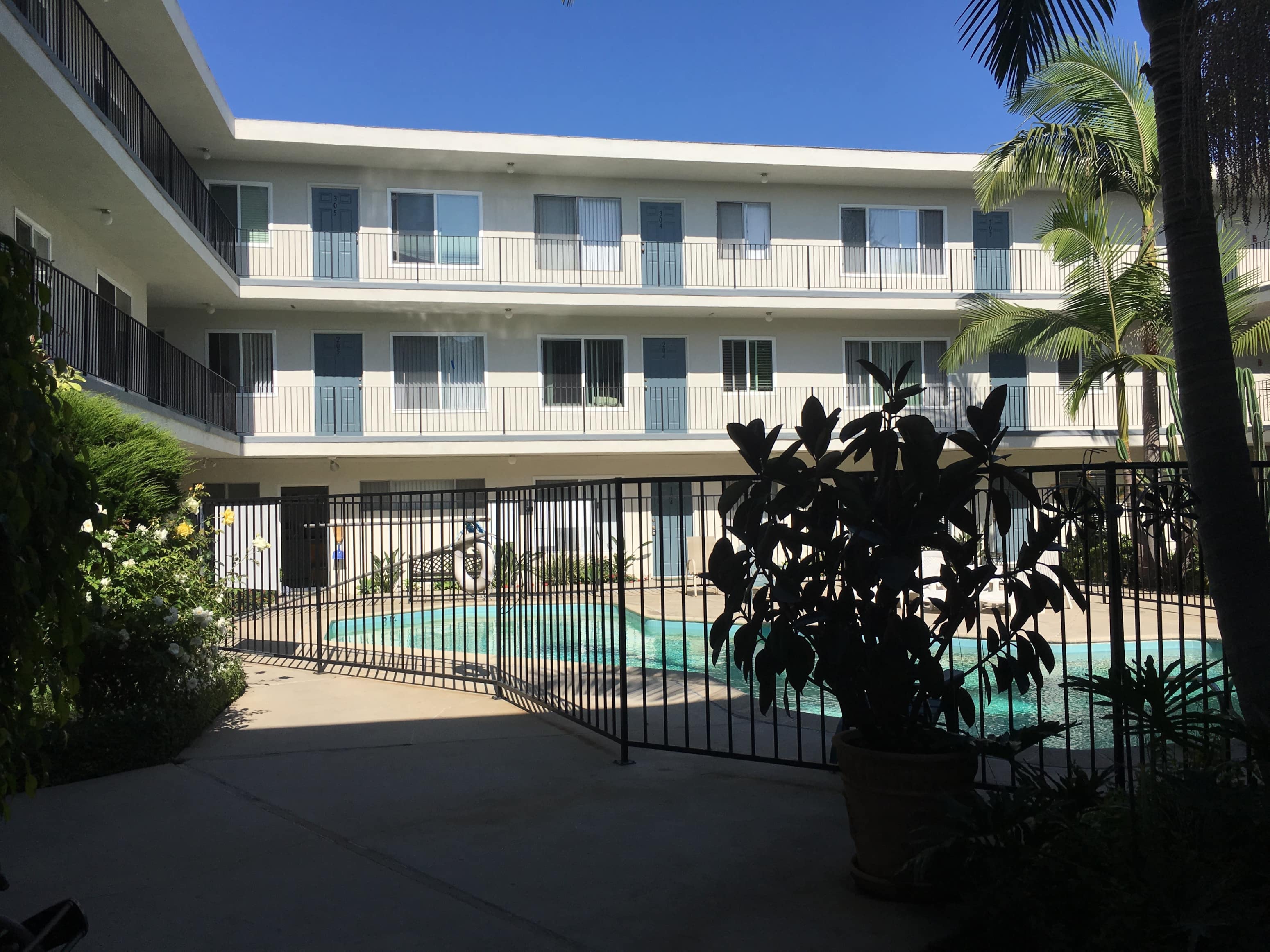 A pool is surrounded by a black fence and a building with balconies.