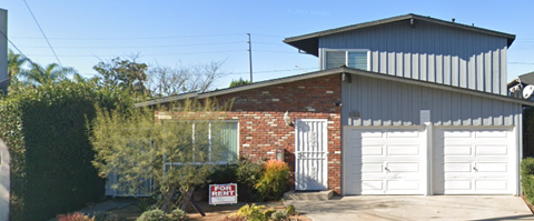 A house with a garage door and a sign in front of it.