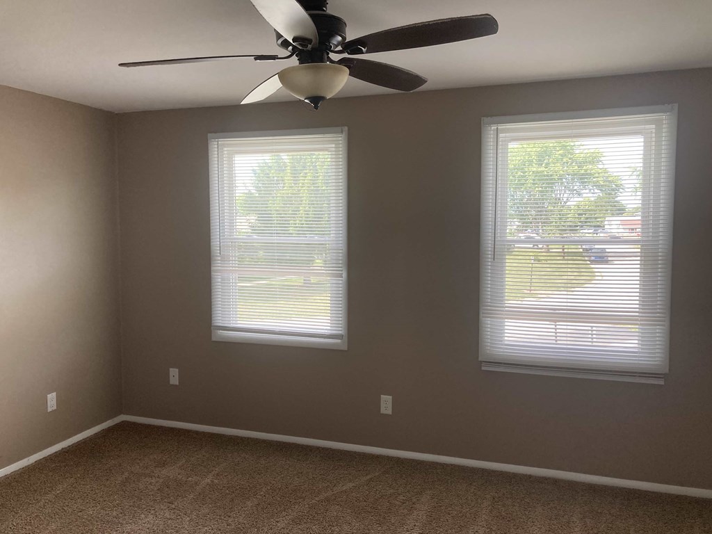 A room with a ceiling fan and two windows.