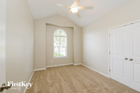 A room with a carpeted floor, a ceiling fan, and a window with a view of trees.