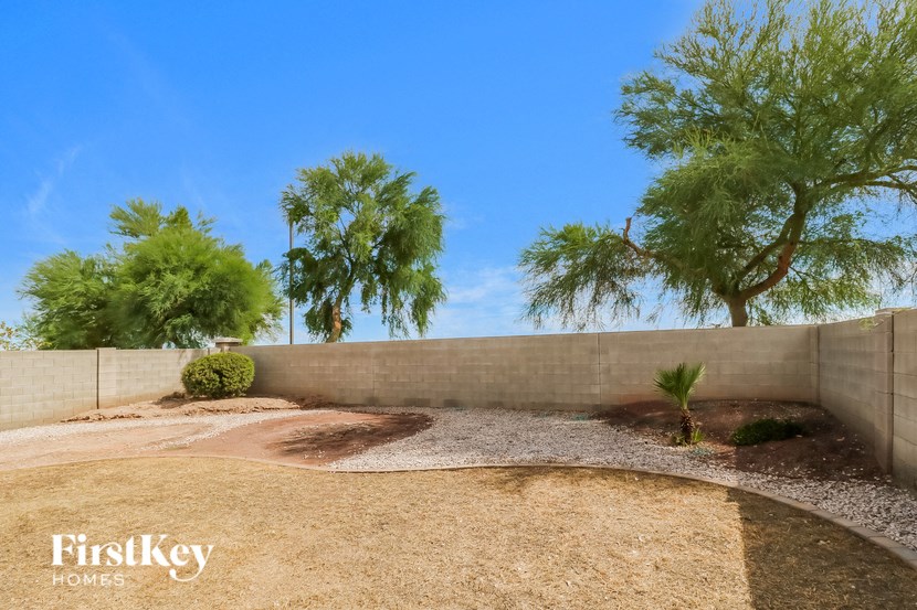 a backyard with gravel and trees and a retaining wall