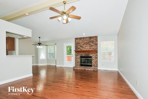 A spacious living room with a brick fireplace and a ceiling fan.