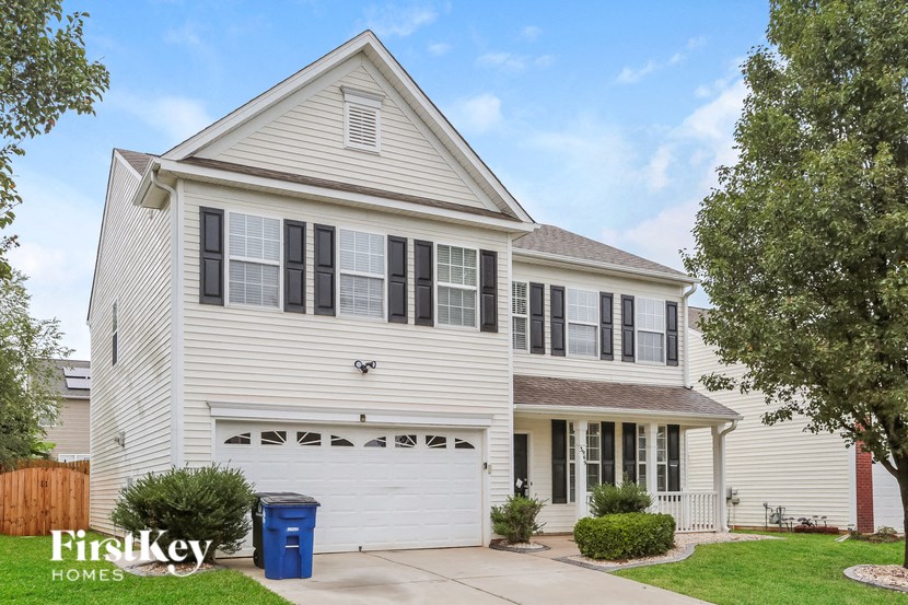 A two-story house with a white garage door and a blue trash bin in front.