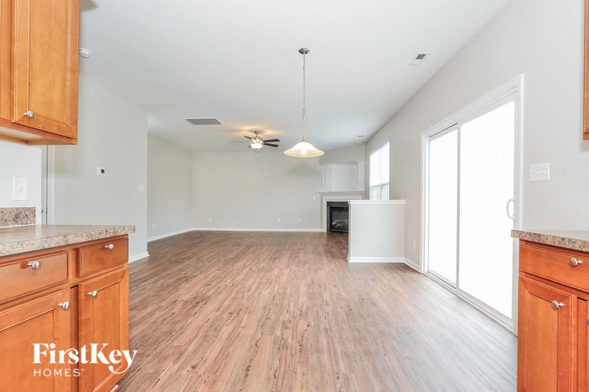 A large empty room with wooden floors and a kitchen area with wooden cabinets.