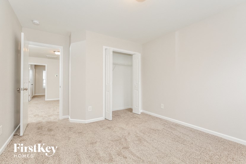 A spacious room with a carpeted floor and white walls, with a doorway leading to another room.