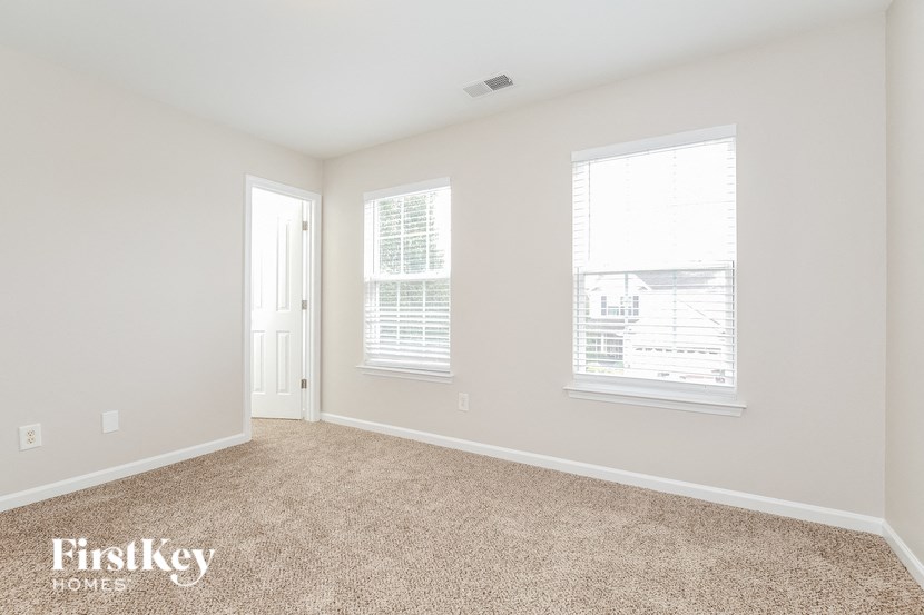A room with a carpeted floor and two windows.