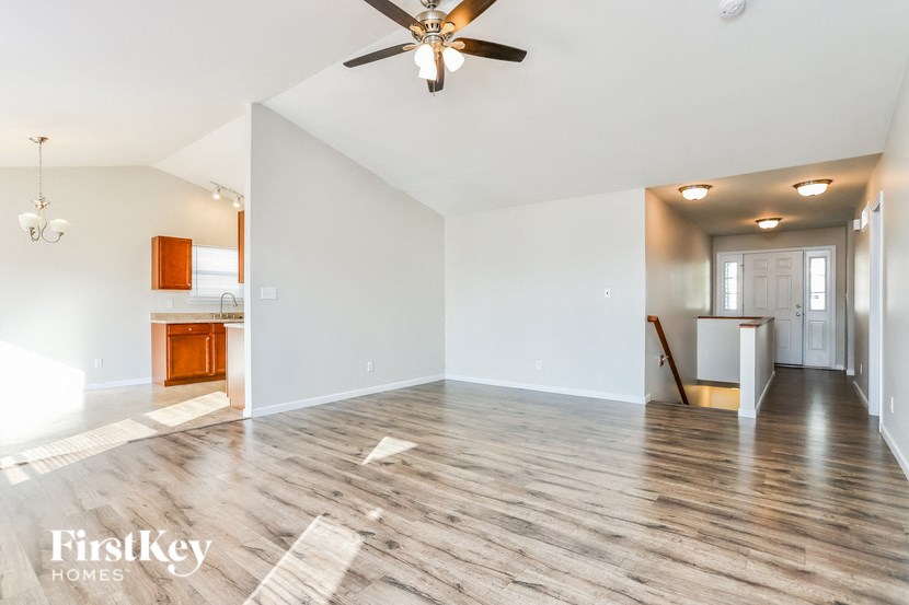 a empty living room with a ceiling fan and a kitchen