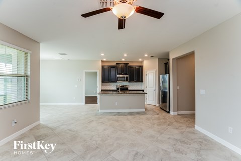 A spacious living room with a kitchen in the background and a ceiling fan above.