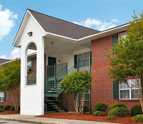 A red brick house with a white front porch and a green staircase.