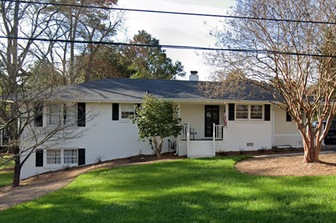 A white house with a black roof and a tree in front.