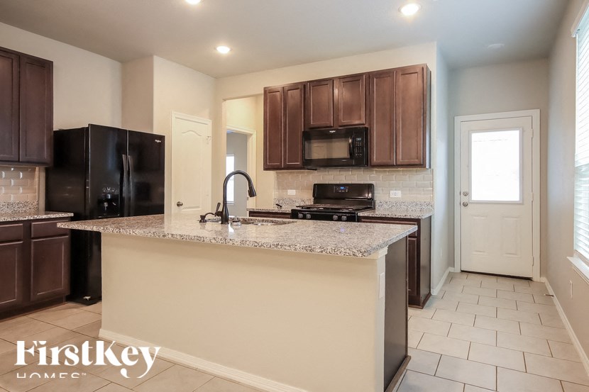 A kitchen with a black fridge and microwave, brown cabinets, and a granite countertop.