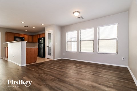 A spacious room with wooden flooring and a kitchen area with a refrigerator, microwave, and cabinets.