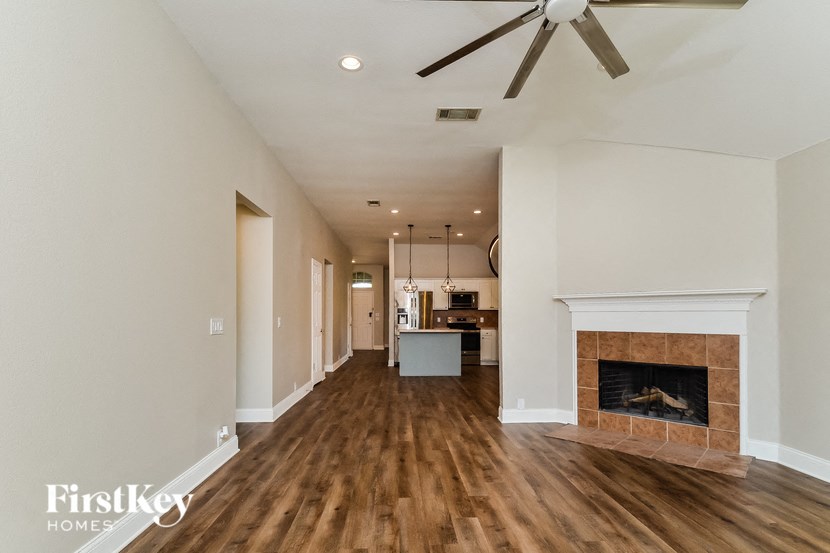 A long, empty hallway with a fireplace and a kitchen in the distance.