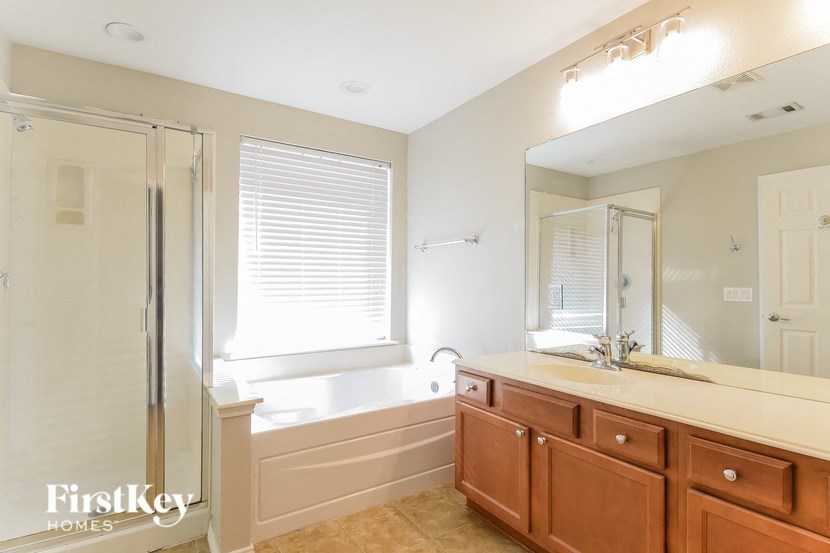 A bathroom with a mirror, sink, and a window with blinds.