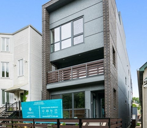 A modern two-story building with a balcony and a sign in front.