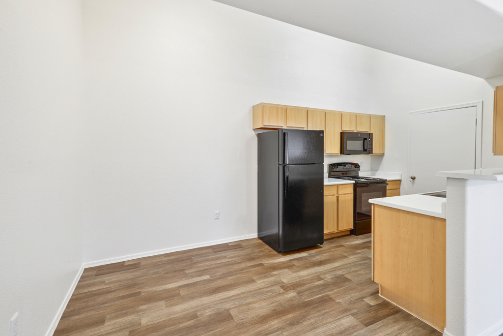 an empty kitchen with a black refrigerator and wooden cabinets