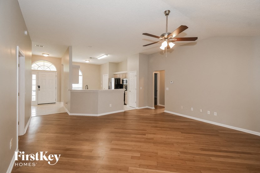 an empty living room with a ceiling fan and a kitchen