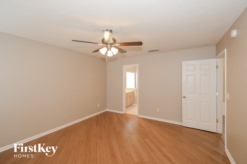 an empty living room with a ceiling fan and a door to a bedroom
