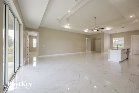an empty living room with a kitchen and a ceiling fan
