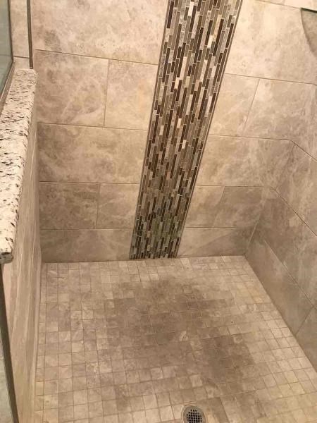 A tiled shower with a marble ledge and a glass block wall.
