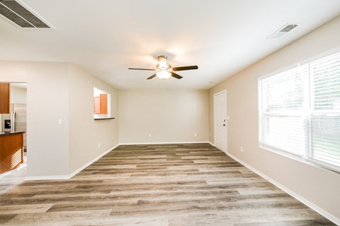 an empty living room with a ceiling fan and large windows
