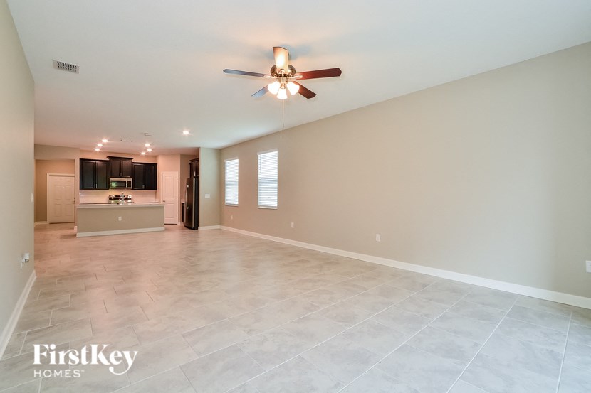 A spacious room with a ceiling fan and a kitchen area in the background.