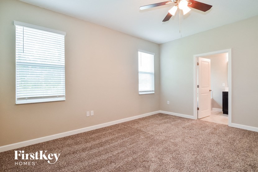 A room with a carpet floor, a ceiling fan, and a door leading to another room.
