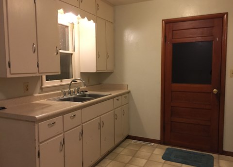 A kitchen with white cabinets and a wooden door.