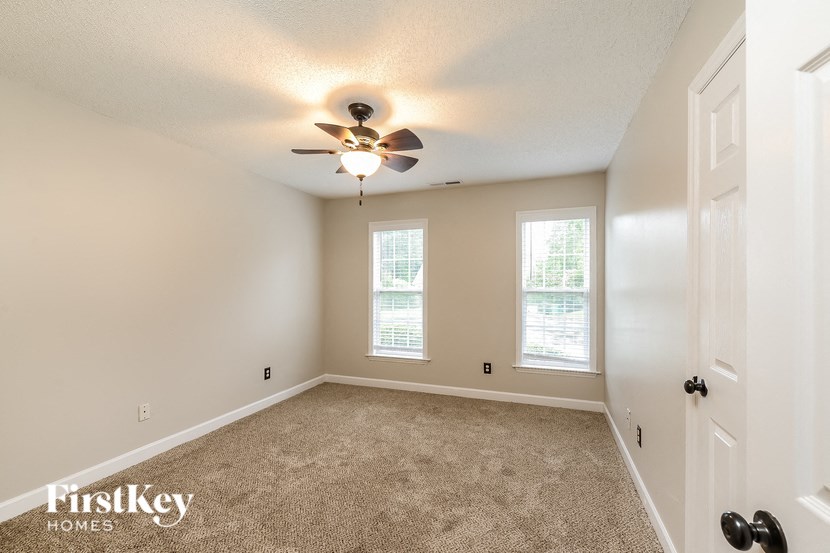 an empty bedroom with a ceiling fan and two windows
