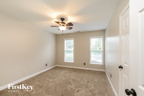 an empty bedroom with a ceiling fan and two windows
