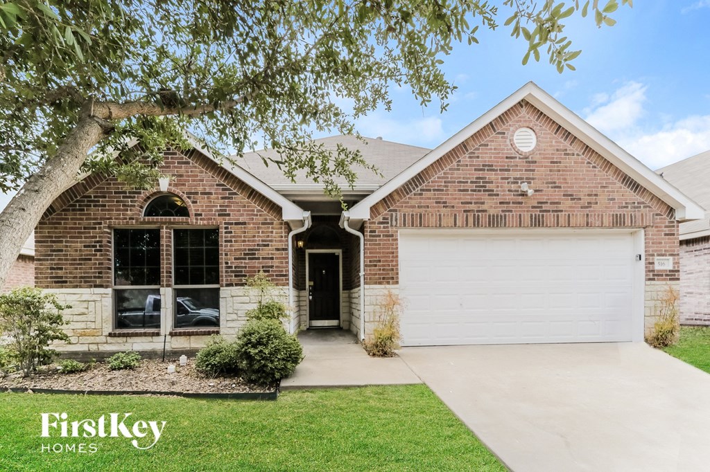 A brick house with a white garage door and a tree in front.