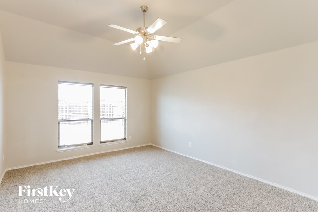 A room with a carpet floor, a ceiling fan, and two windows.