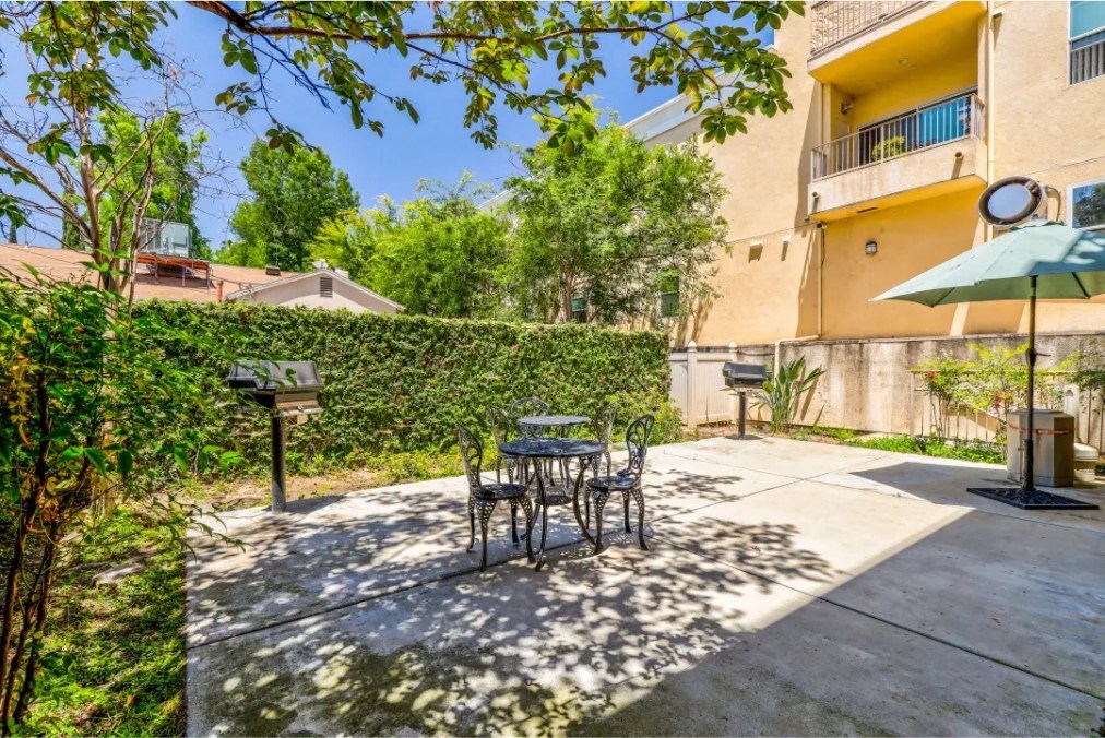 a patio with a table and chairs in front of a hedge