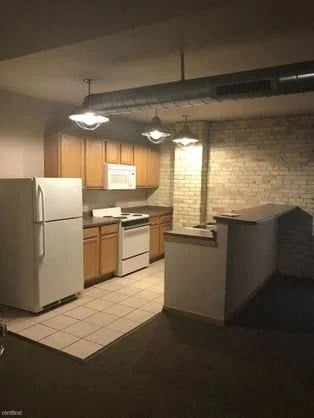 an empty kitchen with white appliances and a brick wall