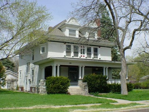 A white house with a grey roof and a tree in front.