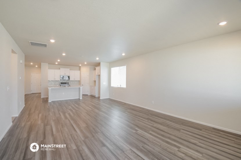 the living room and kitchen of an apartment with white walls and wood flooring
