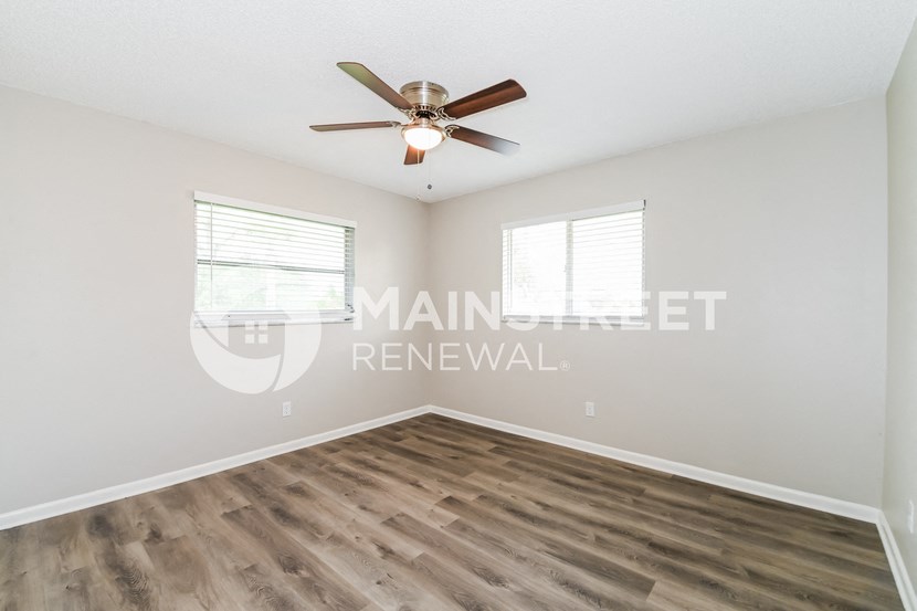 an empty living room with a ceiling fan and two windows