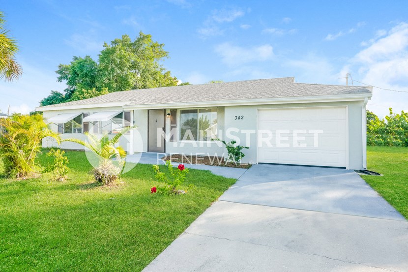 a small white house with a driveway and grass