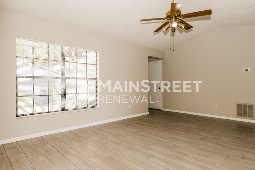 an empty living room with a large window and a ceiling fan