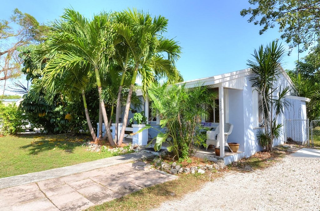 A white house with a porch is surrounded by greenery.