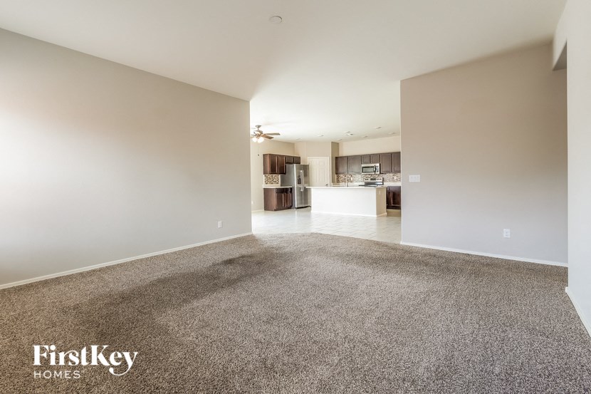 A spacious room with a carpeted floor and a kitchen visible through the open door.
