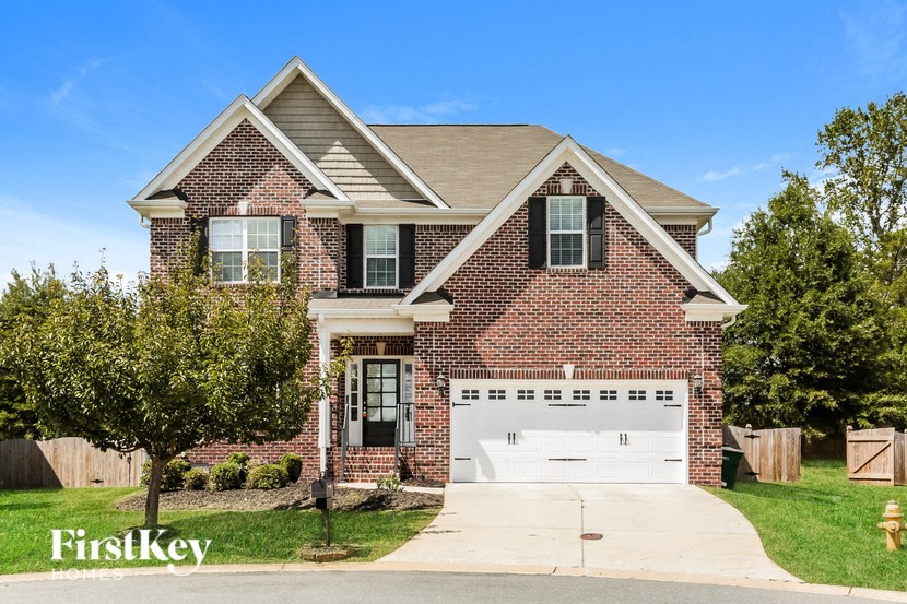 A brick house with a garage and a tree in front.