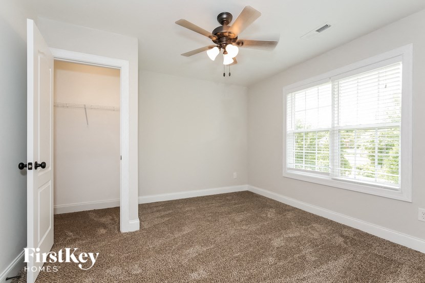 A room with a carpeted floor, a ceiling fan, and a window with blinds.