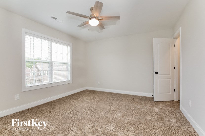 A room with a carpet floor, a ceiling fan, and a door.